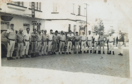 "Diligência Policial. 1972. Praça Lauro Muller. Da esquerda para a direita. Sd Júlio Mikus, Sd Gaúcho (mecânico do batalhão), Sd João de Matos, Cb Tibuski, Sgt Yamazaki, Sgt Bastos, Cb Álvaro, Sgt Emerim, ST Ferraz, Ten Neri dos Santos, Sd Aristeu dos Santos, Sd Vitor Corrêa, Sd Antônio Luiz, Sd Amilton de Lima, Cb Lauro Rocha, Sd Altino Alves e Sd Guilherme."